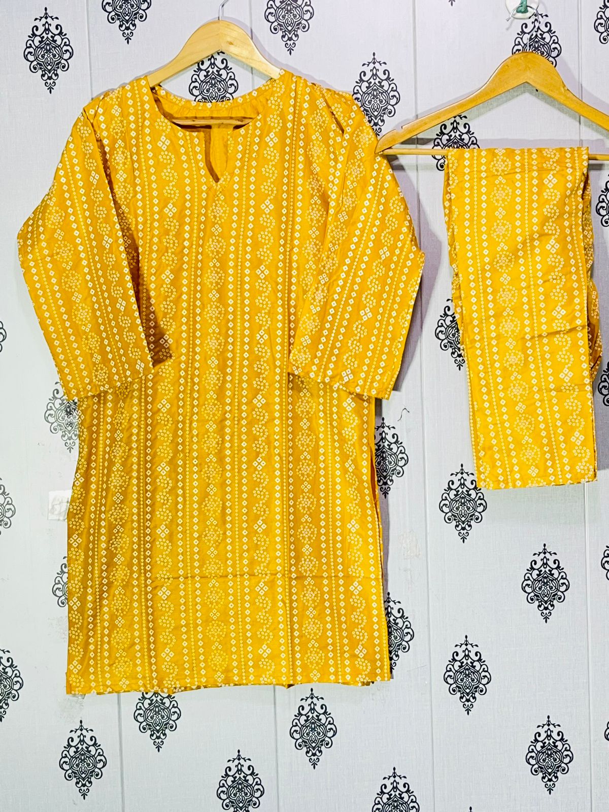 Yellow patterned kurta with matching pants on hangers against a decorative wall.