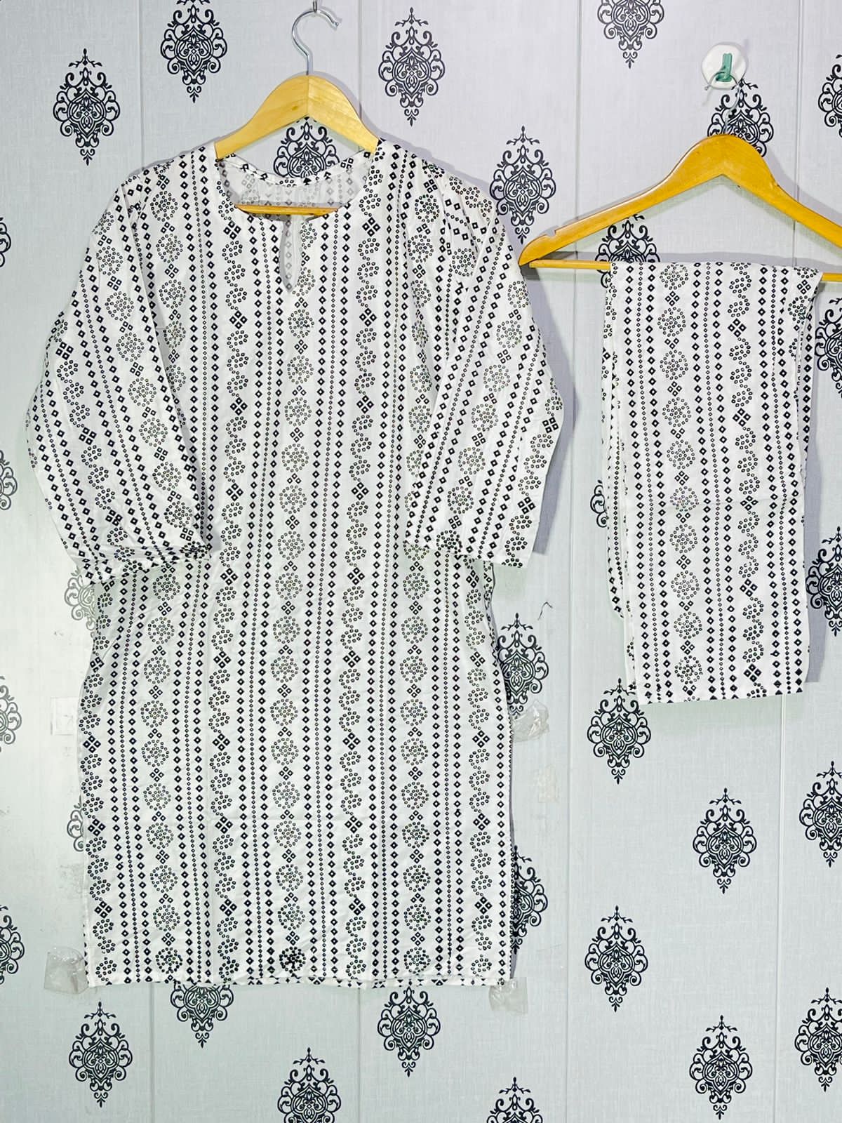 Black and white patterned outfit on hangers against a decorative wall.
