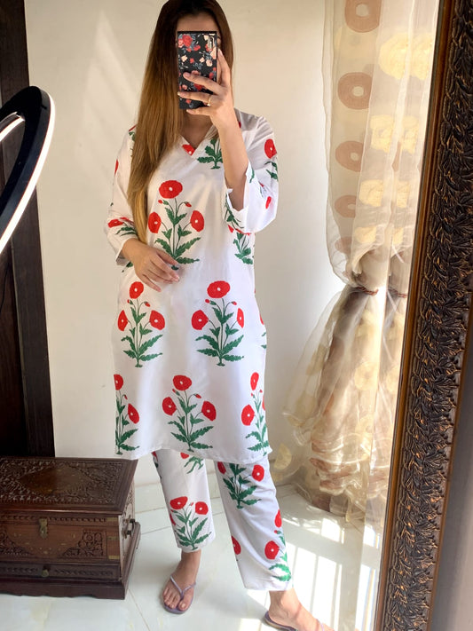 Person wearing a white outfit with red floral patterns in front of a mirror.