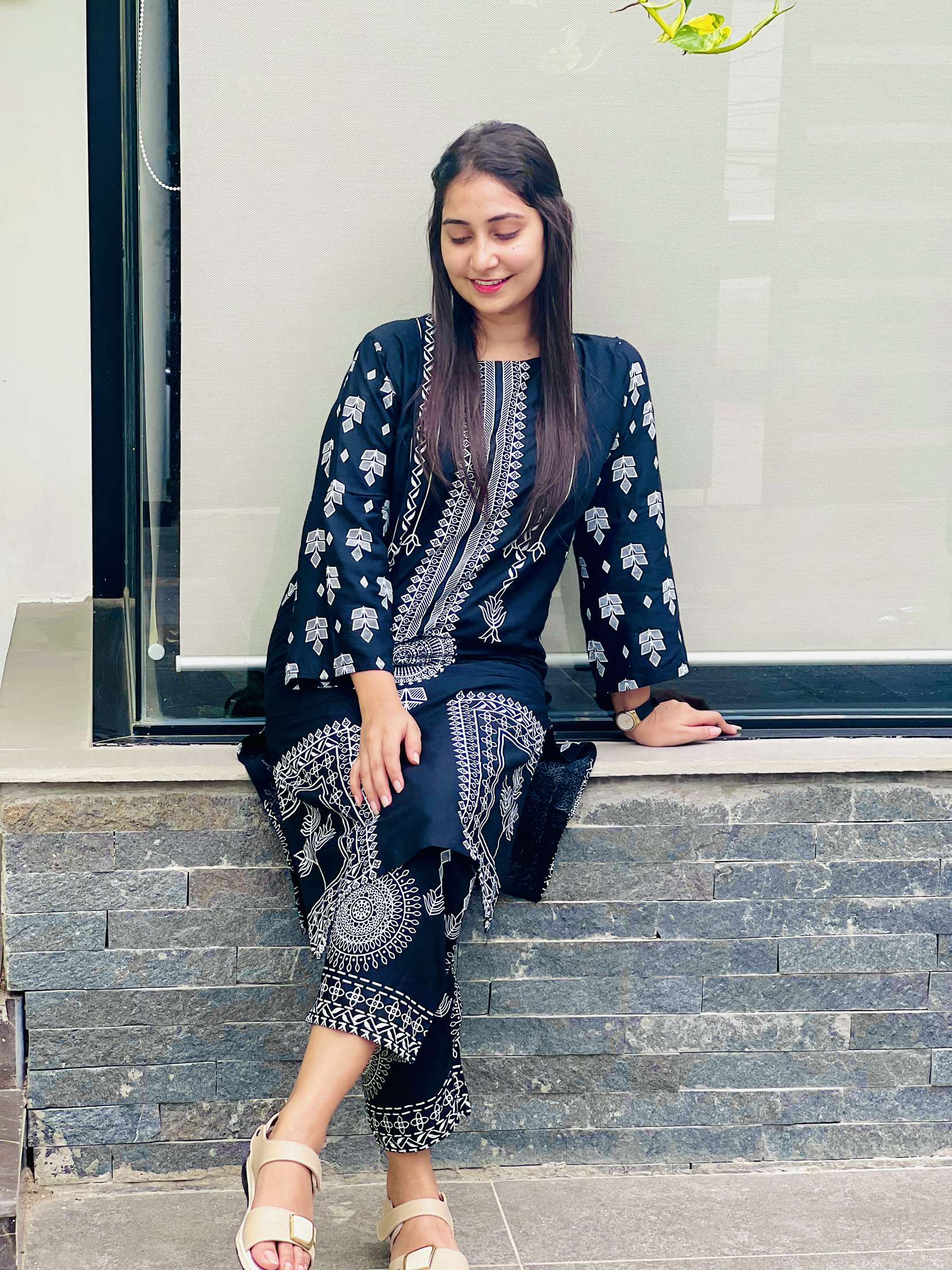 Woman wearing a navy blue traditional outfit with white patterns sitting on steps.