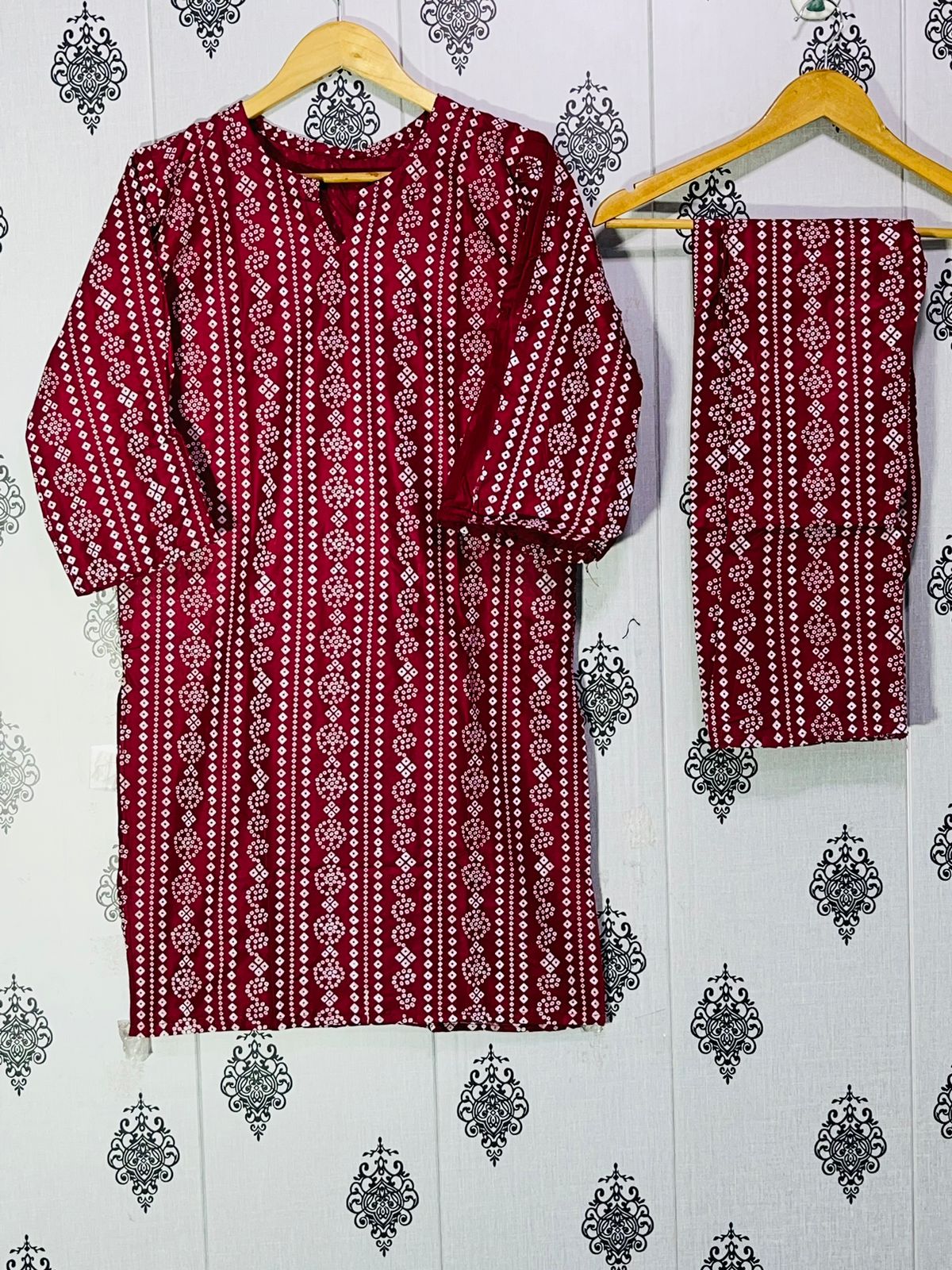 Red and white patterned kurta with matching pants on a hanger against a decorative wall.