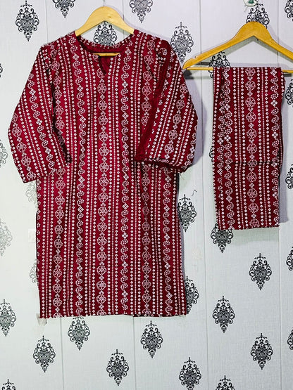Red and white patterned kurta with matching pants on a hanger against a decorative wall.