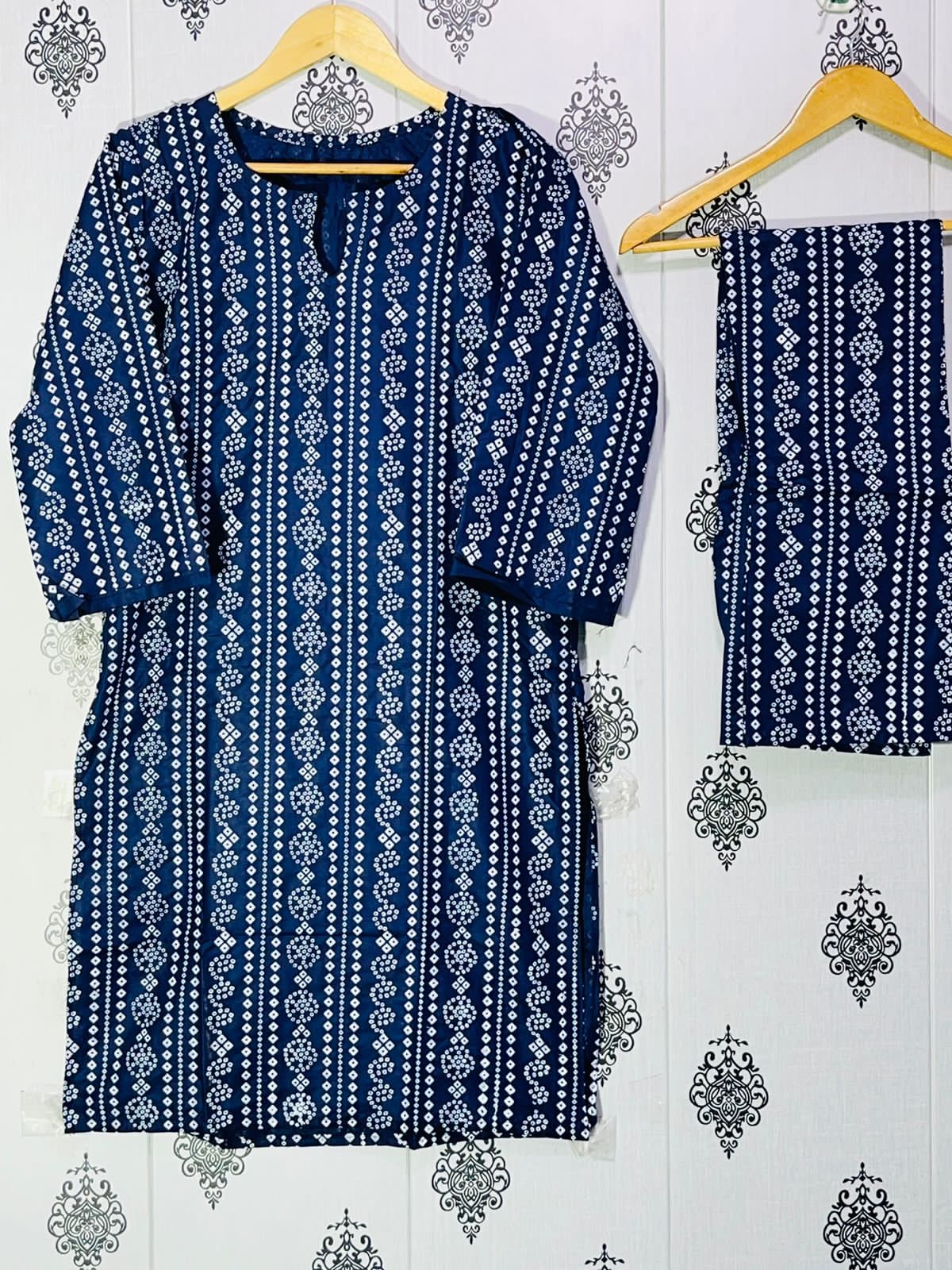 Blue and white patterned dress with matching pants on hangers against a decorative wall.