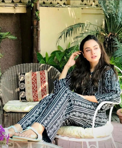 Woman sitting outdoors in a patterned outfit with plants in the background