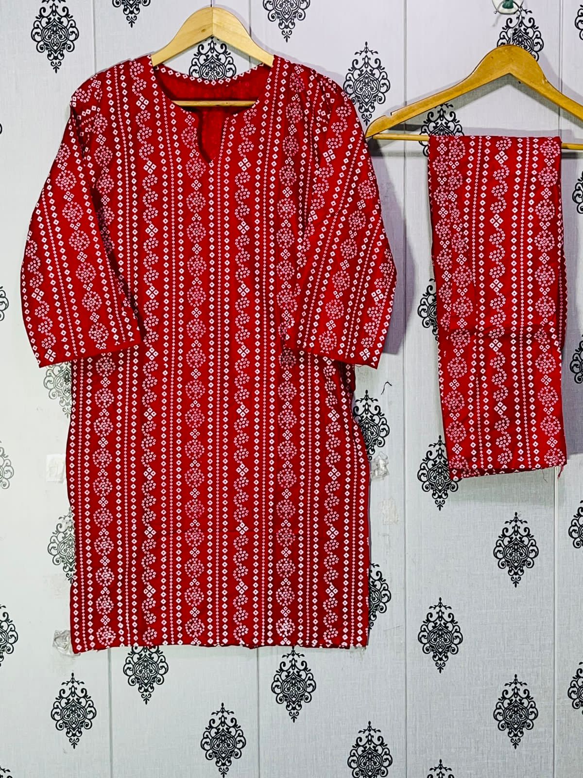 Red and white patterned kurta with matching pants on hangers against a decorative wall.
