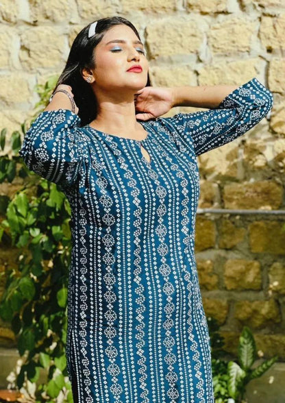 Woman wearing a blue patterned dress standing against a stone wall.