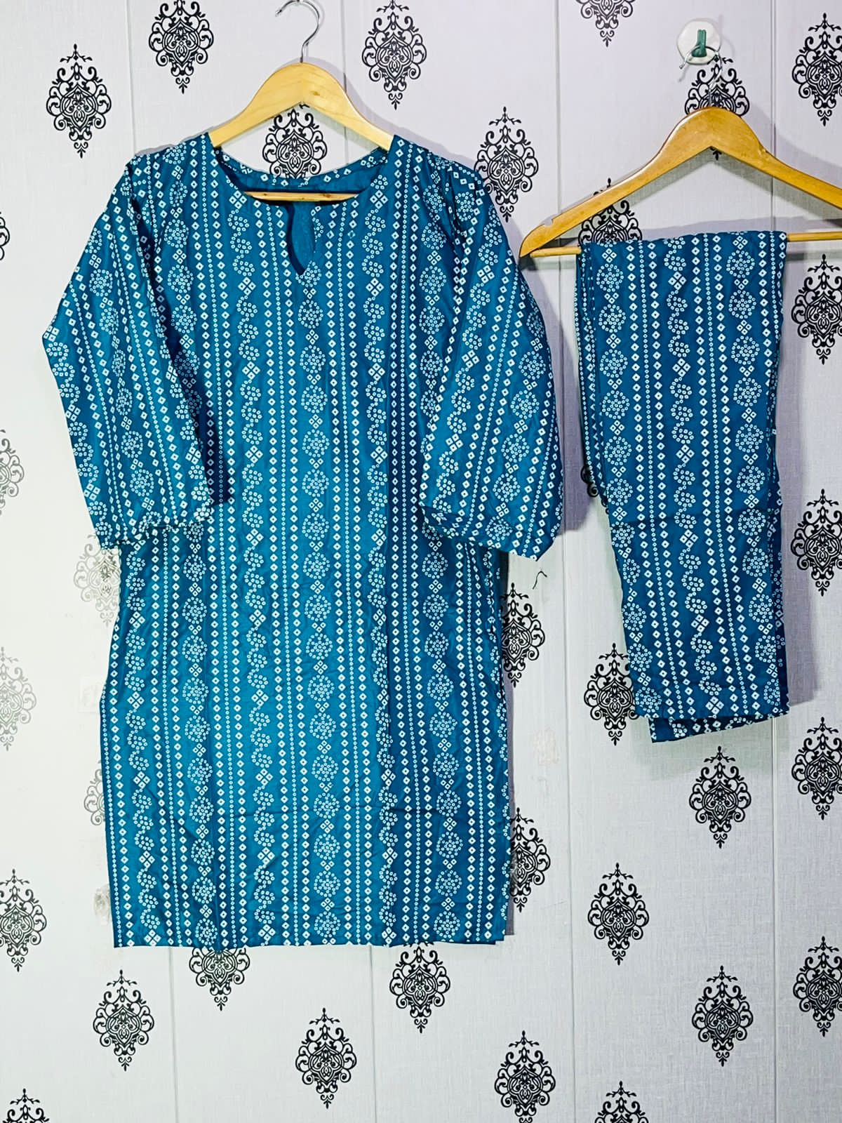 Blue patterned kurta with pants hanging on a wooden hanger against a decorative wall.