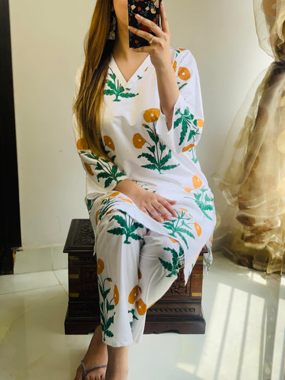 Woman wearing a white dress with floral patterns sitting on a bench.