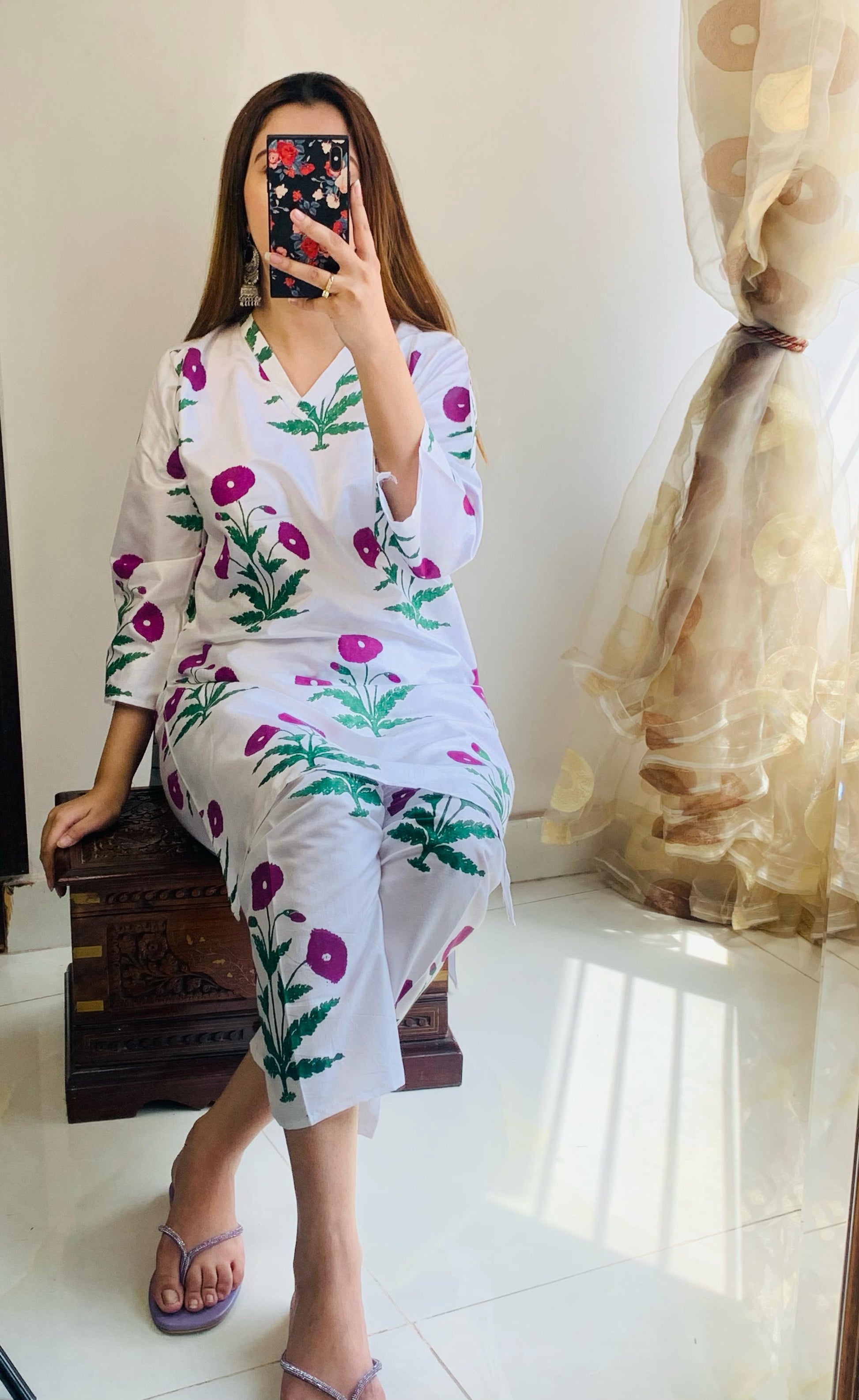 Woman wearing a floral dress sitting on a chair indoors.