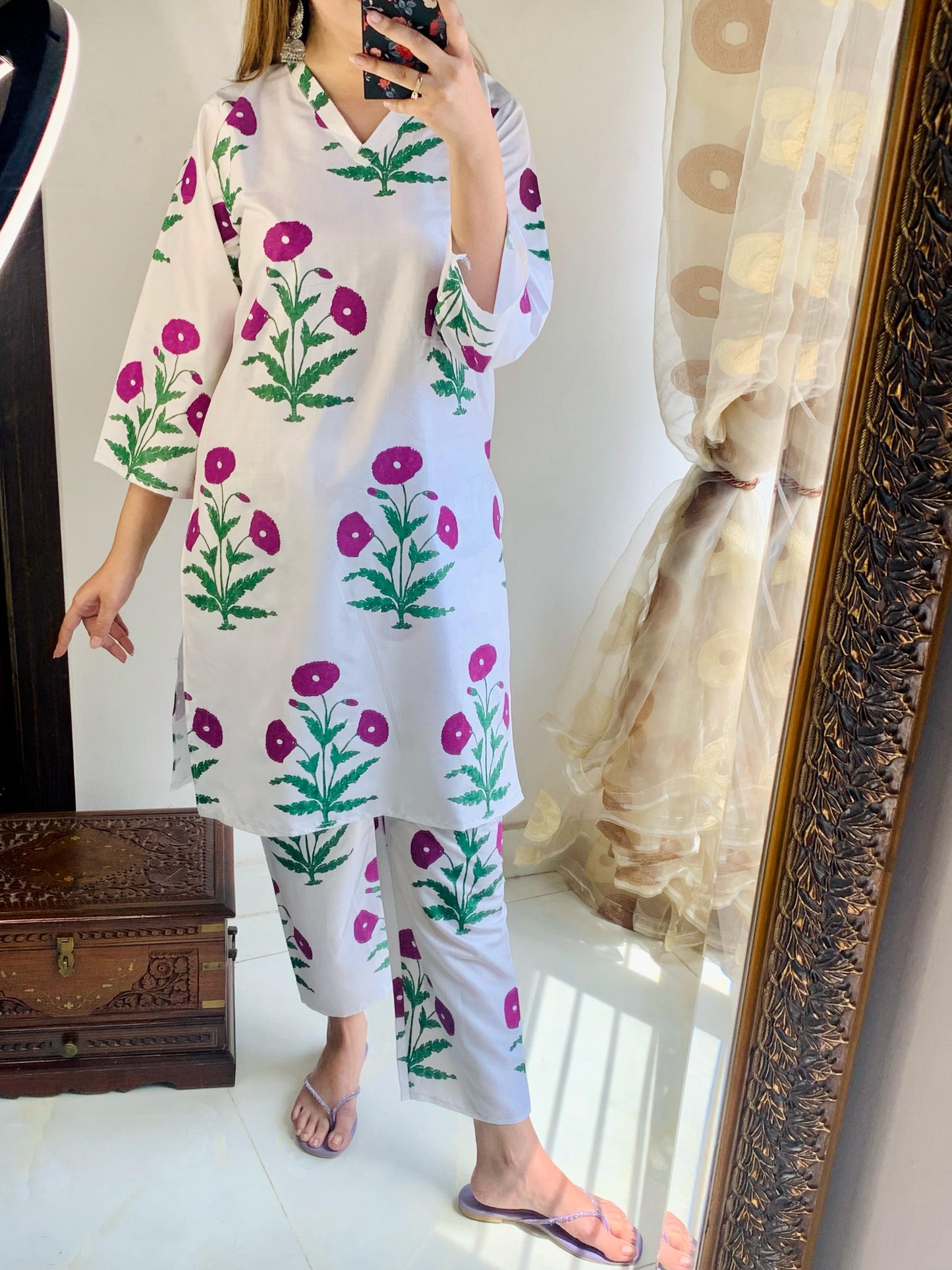 Person wearing a white outfit with floral patterns in front of a mirror.