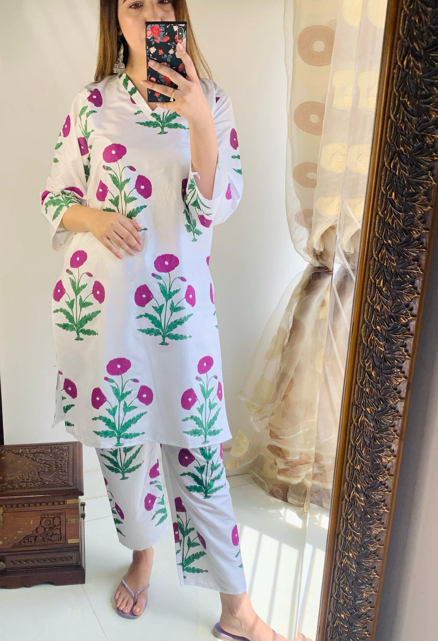 Woman wearing a floral dress and pants standing in front of a mirror.